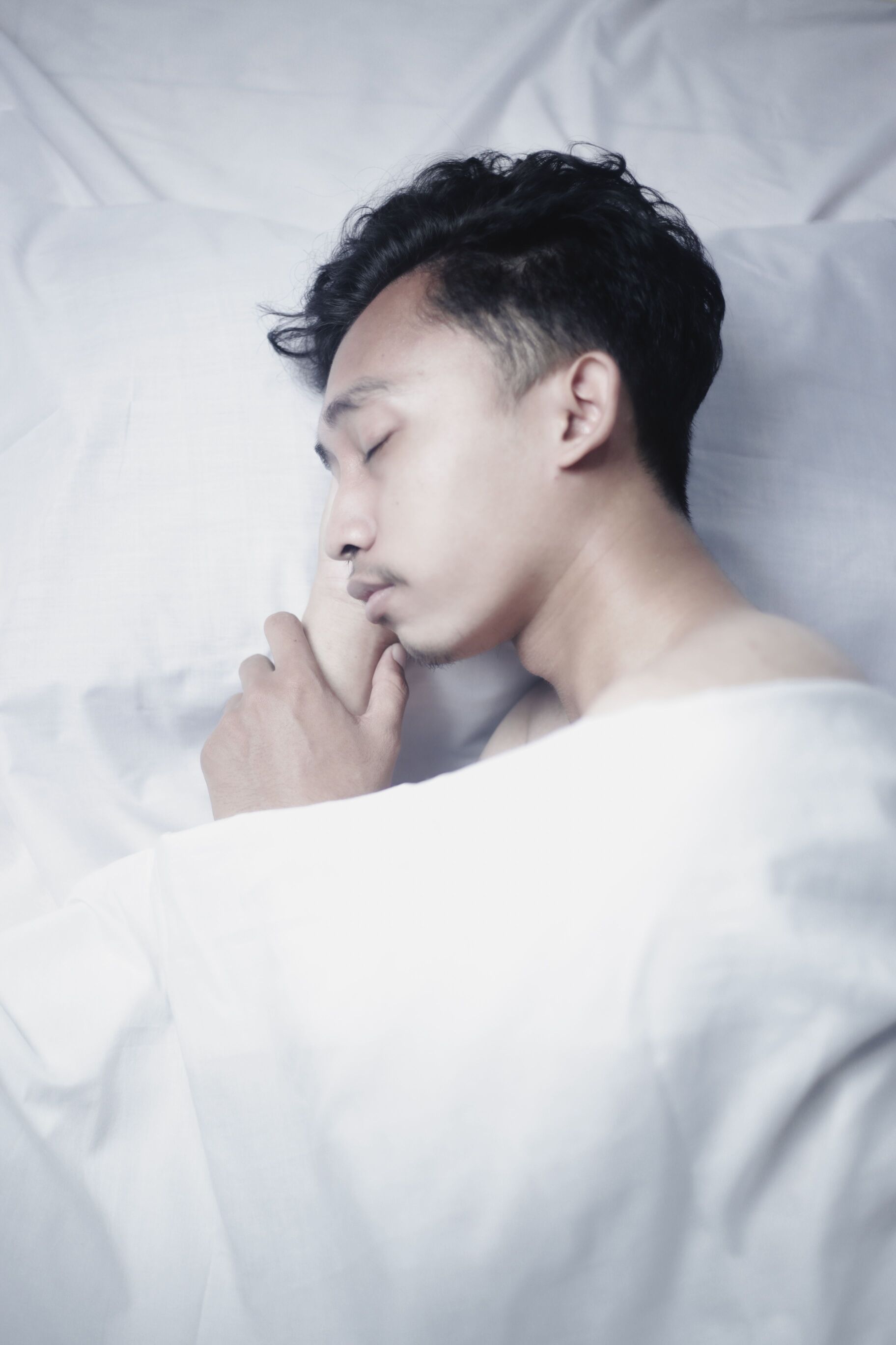 Young man sleeping peacefully on a white pillow under a light blanket